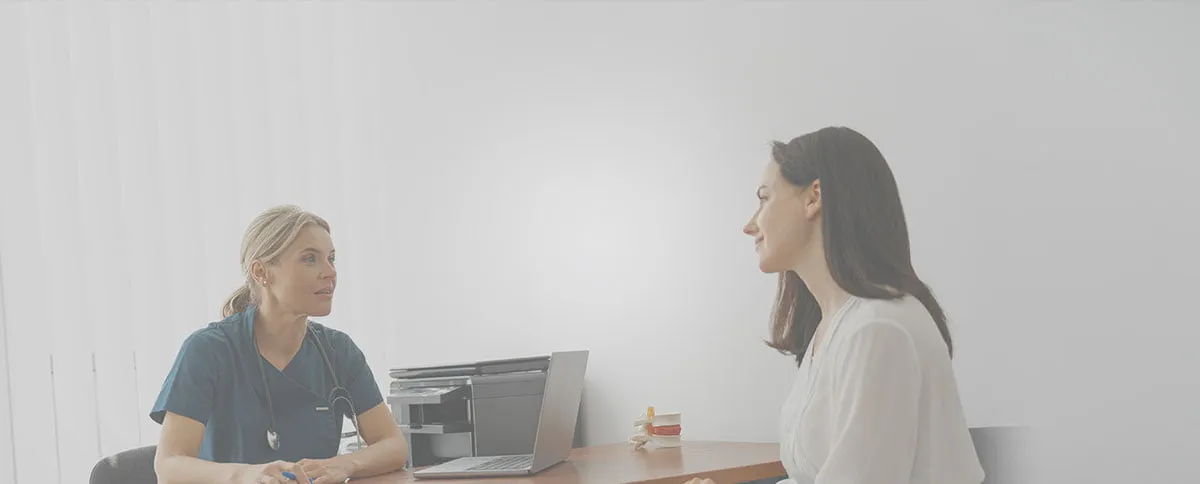 A woman seated at a desk engages in conversation with another woman, both appearing focused and attentive.